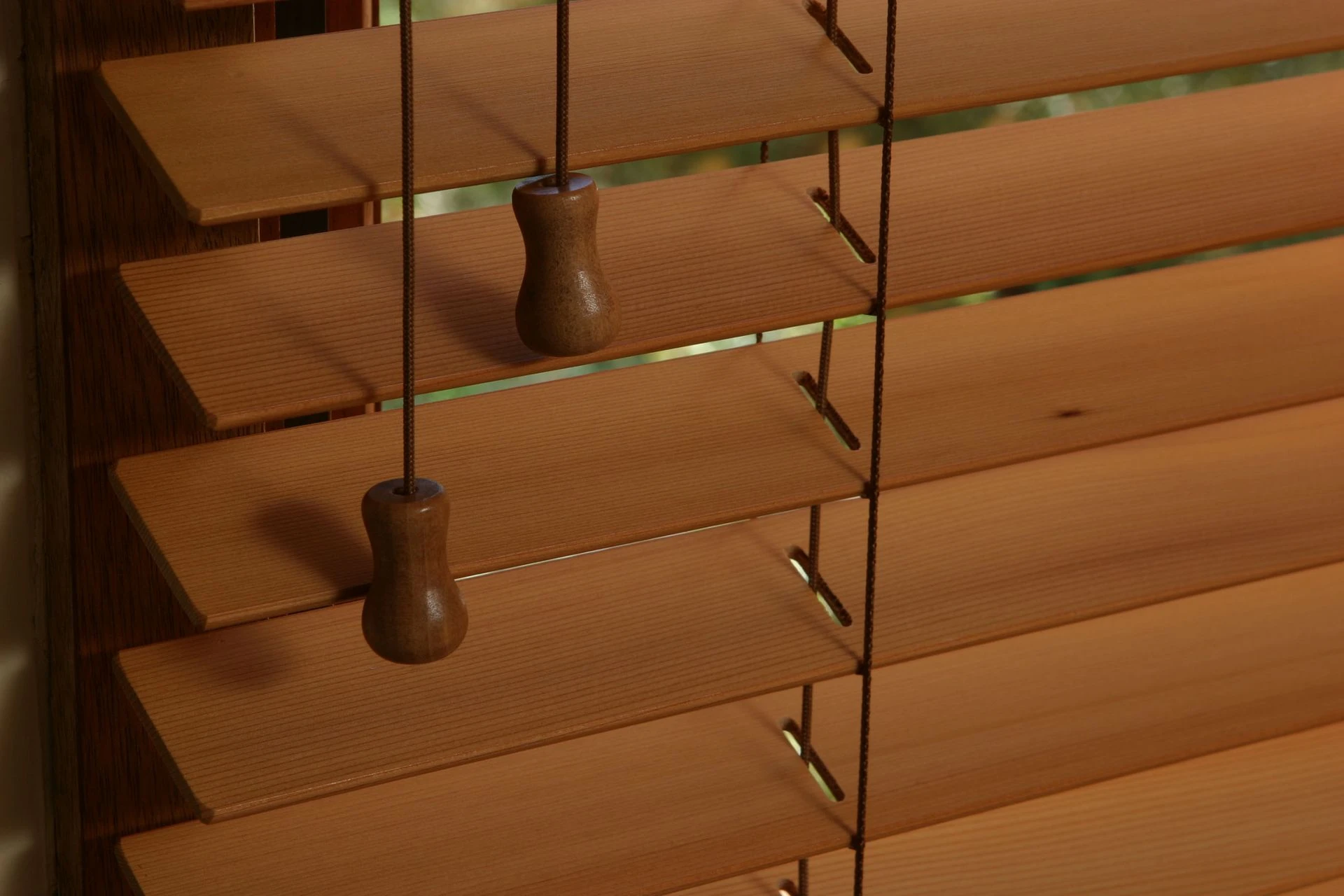 Close crop of timber-look venetian blinds with pull cords, warm sunlight across the slats