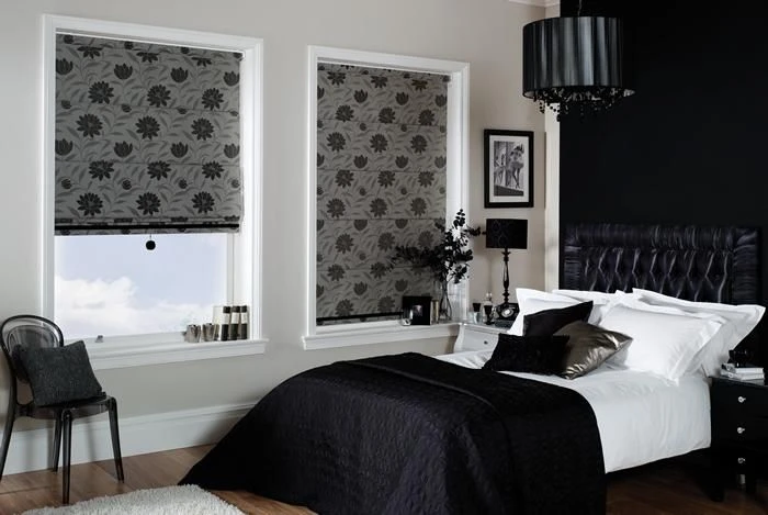 Dark-themed bedroom with black bedding and artwork, two patterned roller blinds on the wall