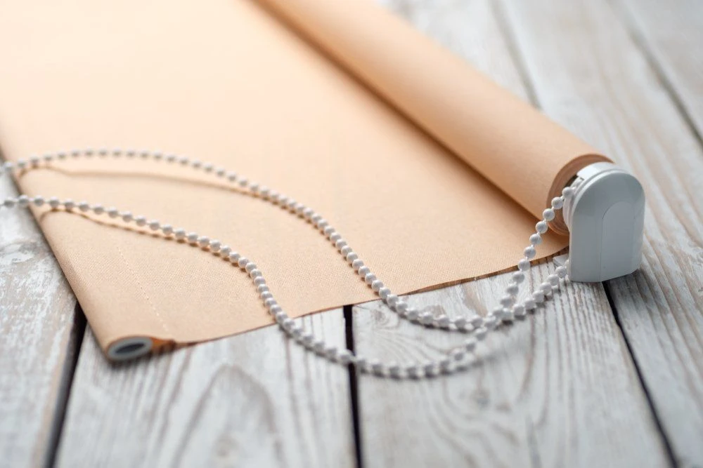 Close-up of a rolled fabric blind sample with chain mechanism on a timber deck
