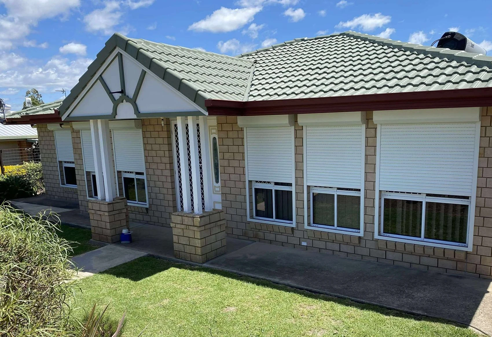 Brick home with white roller shutters fitted across several windows, tiled roof above