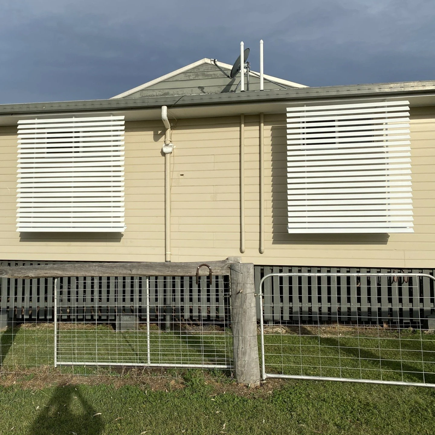 Cream weatherboard house exterior with white plantation shutters on the windows under a stormy sky